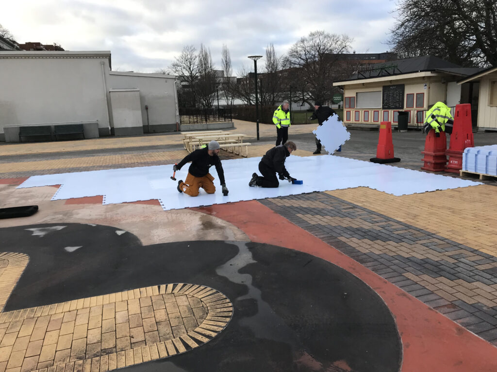 Workers hammer out synthetic ice panels.